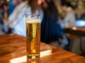 Tall skinny glass of golden lager beer sitting on bar counter