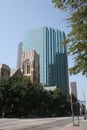 Tall skyscraper with blue glass walls looming over an old stone church beside an empty street