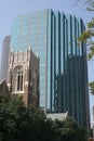 Tall skyscraper with blue glass walls looming over an old stone church beside an empty street