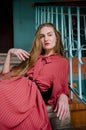 Tall slender caucasian young woman with blond hair in coral dress sitting on concrete stairs of building with blue walls Royalty Free Stock Photo