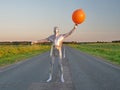 Tall slender man in silver suit is fully dressed in tight silver suit, stands in summer on an empty road, track and holds large