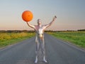 Tall slender man in silver suit is fully dressed in tight silver suit, stands in summer on an empty road, track and holds large