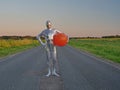 Tall slender man in silver suit is fully dressed in tight silver suit, stands in summer on an empty road, track and holds large