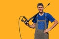 Tall slim guy with a gun for a car wash isolated on yellow background. A worker in coveralls looks at the camera and smiles.