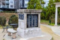 A tall square stone monument with names inscribed in black marble with a black metal table and chair set