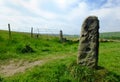 Tall standing stone or old gatepost with old fending and metal gate in pennine pastureland with summer meadows and hillside fields