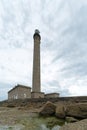 Tall stone lighthouse with rocky shore at low tide under a stormy sky