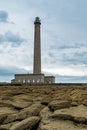 Tall stone lighthouse with rocky shore at low tide under a stormy sky