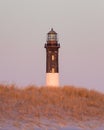 Tall stone lighthouse seen over sand dunes and beach grass with a soft pink sky Royalty Free Stock Photo