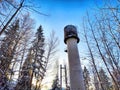 Tall stone lighthouse with surrounding trees under a sunny sky. Majestic water tower Against a Clear Blue Sky in Royalty Free Stock Photo