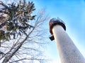 Tall stone lighthouse with surrounding trees under a sunny sky. Majestic water tower Against a Clear Blue Sky in Royalty Free Stock Photo