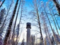 Tall stone lighthouse with surrounding trees under a sunny sky. Majestic water tower Against a Clear Blue Sky in Royalty Free Stock Photo