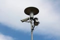 Tall street light on metal post with mounted surveillance camera and various measuring devices on cloudy blue sky back