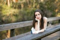 A tall and thin brunette teenager standing and leaning on a park bridge with her head resting on her hands with a Royalty Free Stock Photo