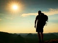 Tall tourist with poles in hand. Sunny evening in rocky mountains. Hiker with big backpack stand on rocky view point above misty v Royalty Free Stock Photo