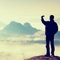 Tall tourist is taking selfie on peak above valley. Smart phone photography