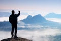 Tall tourist is taking selfie on peak above valley. Smart phone photography