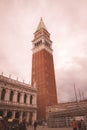 a tall tower with a clock on top of it's side in a city square with people walking around,