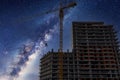 Tall tower crane and buildings and Milky way at night. A construction crane lifts a container for concrete with cement for