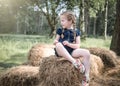 Beautiful cute young girl exploring nature with pig tails hair in shorts on summer day sunshine sitting on bails of hay and straw Royalty Free Stock Photo