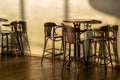 Tall vintage wooden table and chairs stand in a cafe. A light, cool shadow from sunlight reflects on the wall and floor. A clear