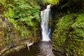 Tall waterfall in a narrow canyon surrounded by green foliage Sgwd Einion Gam