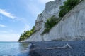 Tall white chalkstone cliffs drop to a rocky beach with a calm ocean and driftwood in the foreground Royalty Free Stock Photo