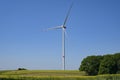 Tall wind turbine with a slender tower and three rotor blades standing on a field in a rural landscape against the blue sky,