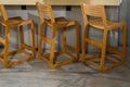 Tall wooden bar stools with backs stand in a row near the bar counter. Natural wood yellow. Close-up. Selective focus. Copy space Royalty Free Stock Photo