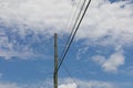 Tall wooden power pole with electrical wires running in three directions, against a beautiful blue sky with clouds Royalty Free Stock Photo