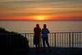 A couple hangs out at the railing watching the sun set..