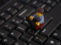 A Lego businessman minifigure sitting on a computer keyboard and working on a laptop