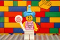 A Lego blue hair girl minifigure with a lollipop against colour brick wall background