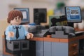 A Lego businessman minifigure sitting on a chair behind a computer in an office