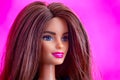 Portrait of Barbie doll with brown hair. Pink background