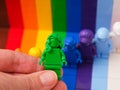 A woman hand holding a green Lego minifigure above other rainbow minifigures. Lego Everyone is Awesome
