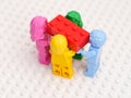 Four monochrome Lego minifigures carrying a red Lego brick