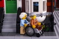 Lego senior couple near his house. Man siting in wheelchair, woman helping him