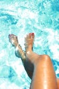 Tan golden legs of young woman and feet painted nails having suntan at swimming pool