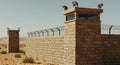 Tan Stone Wall with Barbed Wire and Guard Towers in Arid Desert Royalty Free Stock Photo