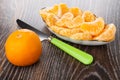Tangerine, table knife, slices of tangerine in plate on wooden table