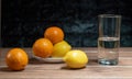 Tangerines and lemons with a water cup on wooden table