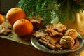 Tangerines and plate with ginger cookies, cinnamon sticks, walnuts on spruce branches background