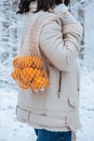 tangerines in a woven bag are held by a young woman in a winter forest Royalty Free Stock Photo