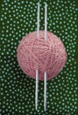 Tangle of pink threads and knitting needles lie a dark green background