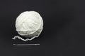 A tangle of white wool threads and a large needle on a black background, accessories for needlework