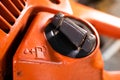 Tank for filling the fuel mixture with oil in the chainsaw. Gas station and lubricant symbol on the body of an orange chainsaw.