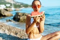 Tanned adorable woman in bikini eating watermelon on sea beach Royalty Free Stock Photo