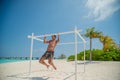 Tanned attractive man making pull ups near ocean in swimming wear at tropical beach at island luxury resort Royalty Free Stock Photo