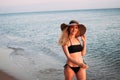 Tanned blonde girl with long hair in a black bikini and a hat smiles and walks along the ocean Royalty Free Stock Photo